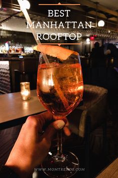 a person holding a wine glass in their hand with the words best manhattan rooftop above it