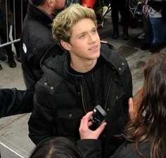 a young man in a black jacket is talking to someone on his cell phone while standing next to other people