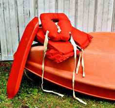 an orange boat is sitting on the grass with two life jackets attached to it's sides