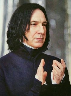 a man with long hair wearing a black suit and holding his hands together in front of him