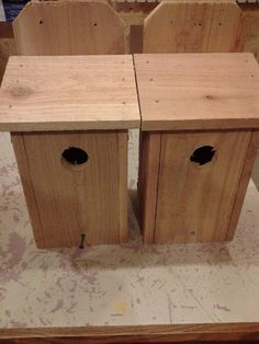 two wooden birdhouses sitting on top of a table next to each other with holes in them