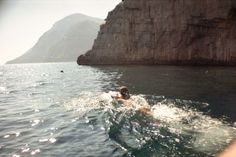 a person swimming in the ocean near a cliff