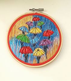 an embroidery project with colorful umbrellas in the rain on a white wall behind it