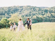 a bride and groom walking through tall grass with their children