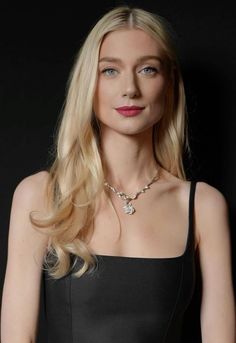 a woman with long blonde hair wearing a black dress and posing in front of a black background