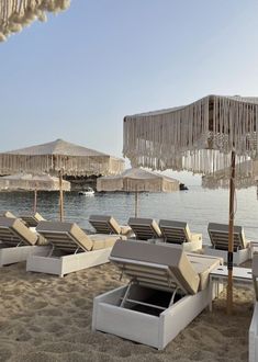 lounge chairs and umbrellas on the beach with water in the backgroung