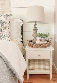 a white nightstand with a basket on it next to a bed