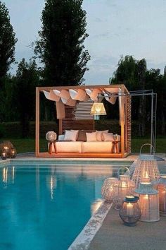 an outdoor living area next to a swimming pool with lit candles on the floor and furniture