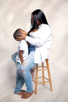 a woman sitting on top of a stool next to a little boy who is touching his face