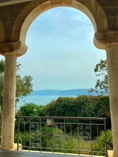 an open window looking out at the ocean and mountains from a building with columns in front of it