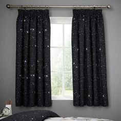 a bedroom with black curtains and stars on the window sill, in front of a bed