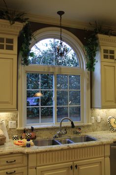 a kitchen with white cabinets and an arched window above the sink is decorated with greenery