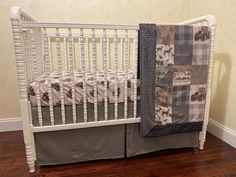 a white crib with a quilted blanket on the top and bottom rail, next to a wooden floor