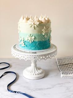 a blue and white frosted cake sitting on top of a table next to a ribbon