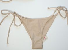 Get ready to hit the beach in style with our Isla Bikini Bottom! Featuring a chic beige color and side-tie design, this bikini bottom will flatter your figure and add a touch of elegance to your swimwear collection. Perfect for a day of fun in the sun, make a statement with our Isla Bikini Bottom! Our versatile collection is eco-friendly! It is produced with the Amni® Soul Eco, the world’s first biodegradable yarn, has an enhanced polyamide 6.6 formula allowing clothes to quickly decompose after being properly discarded. This technology keeps the durability and quality of the garments while still offering the polyamide fiber benefits (soft touch, comfort, easy care, etc.) Degrading in around three years*, the Amni® Soul Eco solution decomposes ten times faster than conventional polyamides Chic Beige Swimwear For Poolside, Beige Beachwear Bottoms For Beach Season, Chic Beige Stretch Swimwear, Summer Beach Bottoms In Neutral Color, Neutral Summer Bottoms For Beach, Neutral Summer Beach Bottoms, Chic Beige Swimwear For Beach Season, Chic Beige Swimwear For Beach, Beige Beachwear Bottoms For Pool