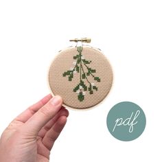 a hand holding up a small cross stitched christmas tree ornament in front of a white background