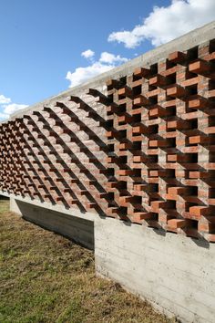 a wall made out of red bricks on the side of a building with grass and blue sky in the background