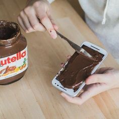 a person holding a cell phone with chocolate spread on it next to a jar of nutella