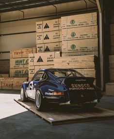 an old race car sits on a pallet in front of stacks of wood boxes