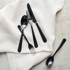 three forks, two spoons and one knife on a white napkin with black handles