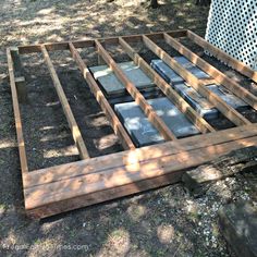 a wooden frame with several pieces of glass on it in the dirt near trees and bushes