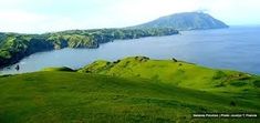 an island in the middle of water surrounded by green hills and grass on both sides