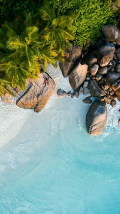 an aerial view of the water and rocks at a beach with palm trees in the background