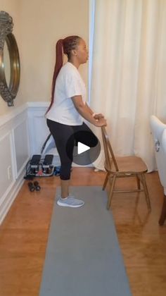 a woman standing on top of a yoga mat in front of a mirror and chair