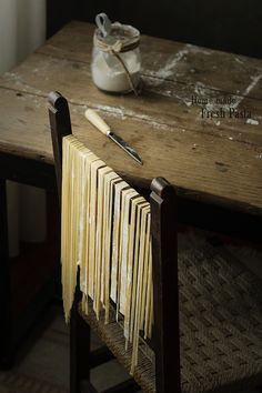 a wooden table topped with books and a pair of scissors next to a jar filled with pasta noodles