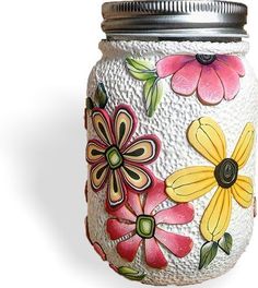 a painted mason jar with metal lid and flower designs on it's side, sitting against a white background