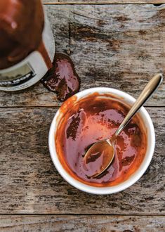 a bowl filled with sauce next to a bottle of ketchup on top of a wooden table