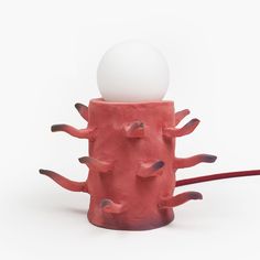 a red and white object sitting on top of a wooden table next to a light bulb