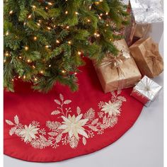 a christmas tree skirt with presents under it on a red tablecloth next to a small christmas tree