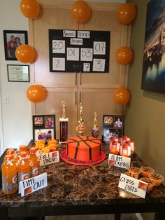 a table topped with an orange cake covered in candies and balloons next to pictures on the wall