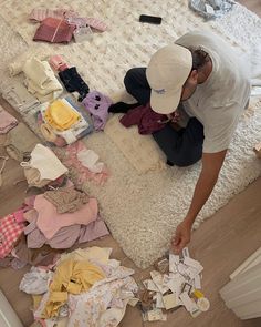 a man sitting on the floor surrounded by clothes and other items that are scattered around him