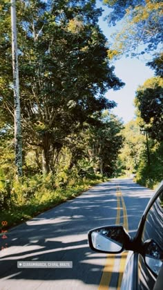 a car is driving down the road with trees in the back ground and on the side