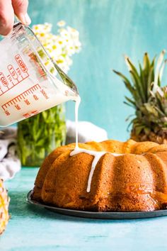 someone pours milk into a bundt cake on a blue table with pineapples in the background