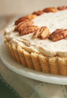 a cake with white frosting and nuts on top sits on a plate, ready to be eaten