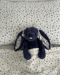 a blue stuffed animal sitting on top of a bed next to two pillow cases with white and blue flowers