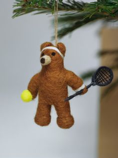 a teddy bear ornament hanging from a christmas tree with a tennis racket and ball