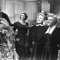 three women standing next to each other in front of a christmas tree with decorations on it