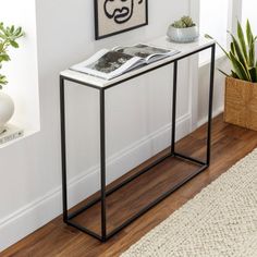 a black and white console table with a magazine on it's shelf next to a potted plant