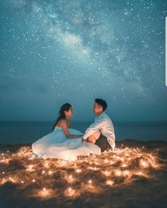 a man and woman sitting on the ground under stars