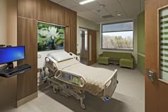 a hospital room with a bed, television and green couch in front of a large window