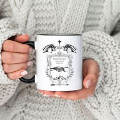 a woman holding a white and black coffee mug in her hands with an image of a bat on it