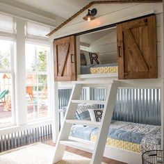 a bunk bed with a ladder to the top and some pillows on it in front of two windows