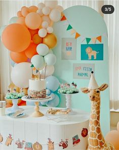 a giraffe standing in front of a table with balloons and cake on it