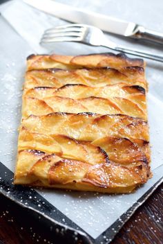 a square pastry sitting on top of a metal tray next to a knife and fork