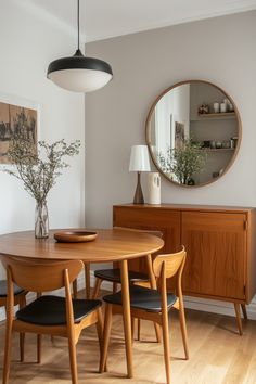 a wooden table with four chairs and a round mirror on the wall in a dining room