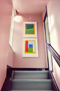 two paintings hang on the wall next to stairs in a house with pink walls and black trim